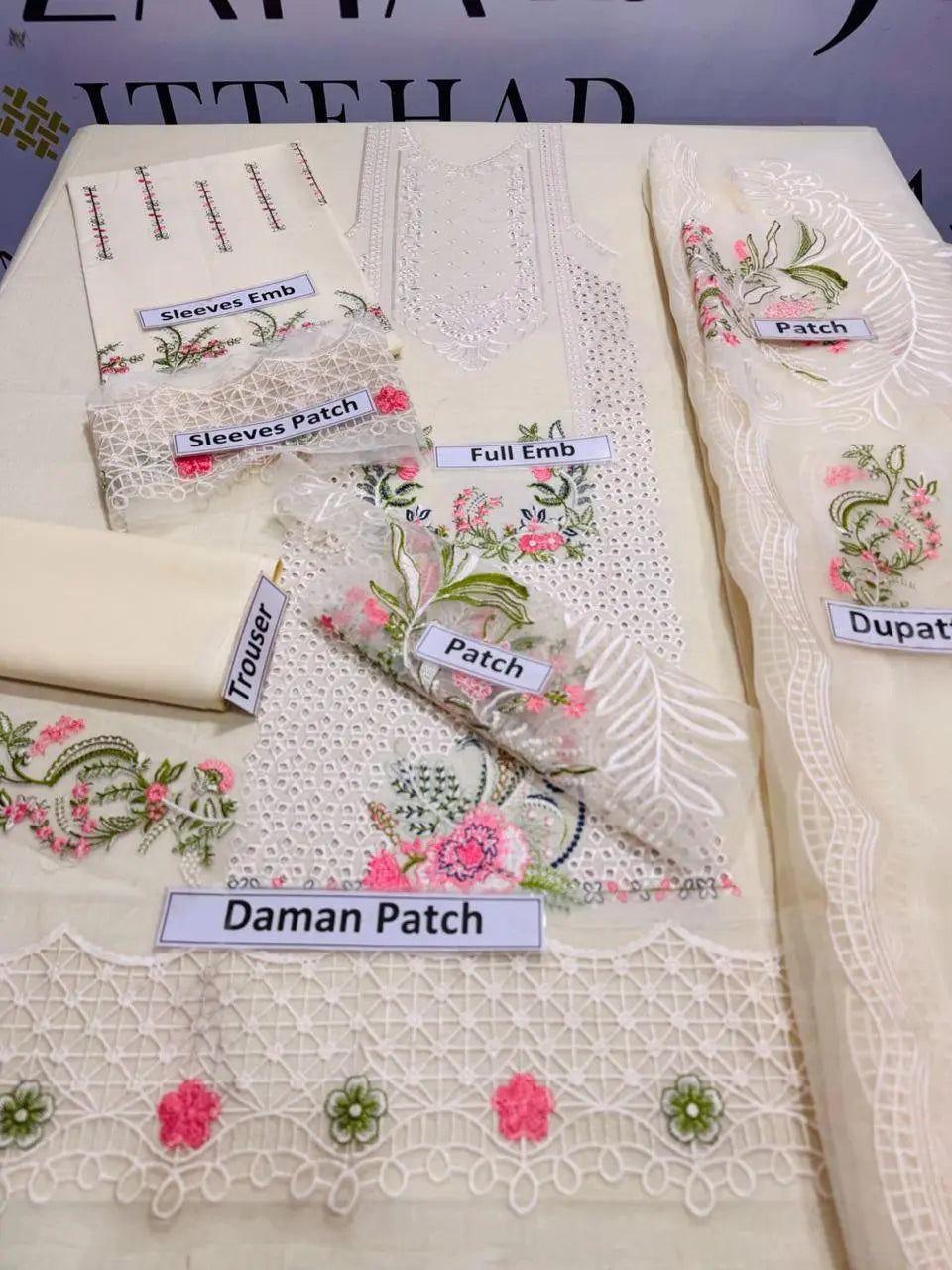 Off white unstitched embroidered women's suit set, including floral lace patches, sleeves, dupatta, and trouser pieces.