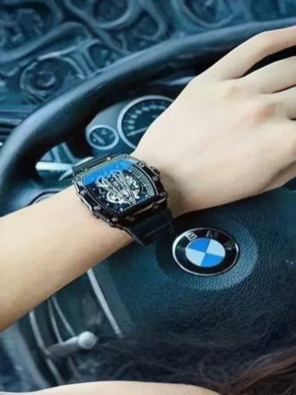 Hand wearing a luxurious watch on a car dashboard with a BMW logo.
