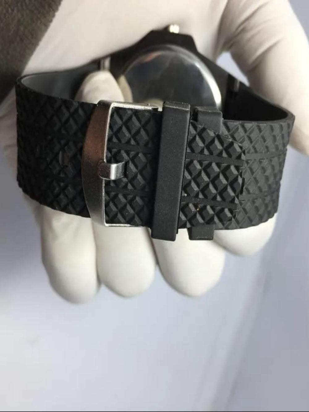 Black textured belt with silver buckle held by a gloved hand on a light gray background