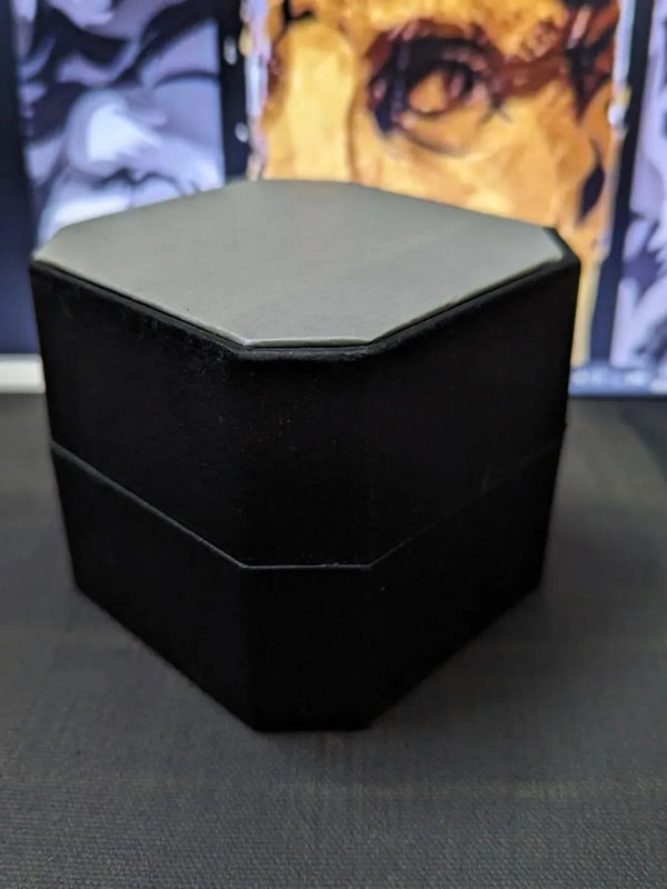 Black hexagonal jewelry box on a dark surface with a blurred background